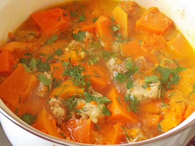 The pumpkin and pork stew simmering gently in a pot A pot of pumpkin and pork stew simmering on the stove, with the pumpkin chunks visible.