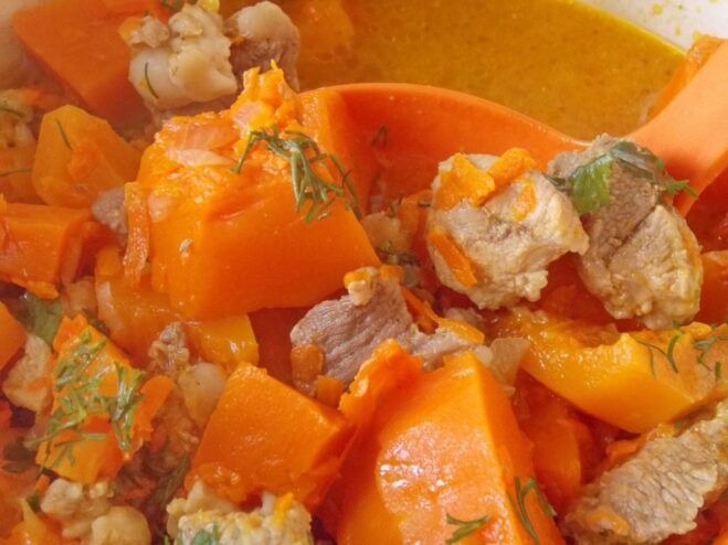 Gently stirring the pumpkin and pork stew in a pot A spoon stirring the pumpkin and pork stew in a large pot on the stove.