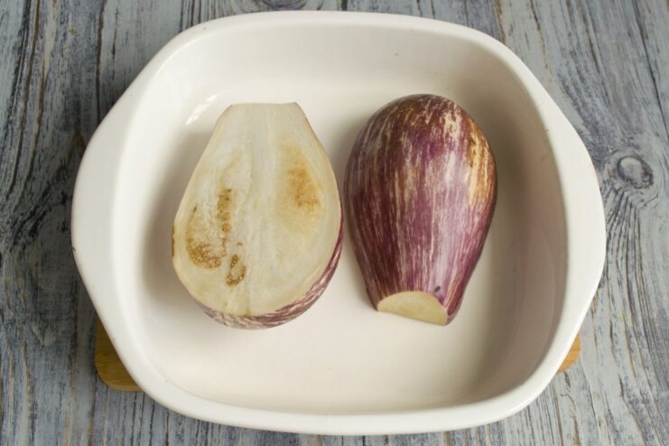 Step 1: Preparing the Eggplants for Stuffing A whole eggplant next to one that has been sliced in half lengthwise on a cutting board.