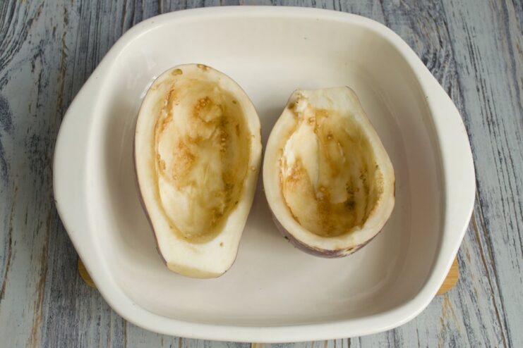 Creating Eggplant 'Boats' for the Filling Using a spoon to scoop the flesh out of an eggplant half, creating a hollow shell.