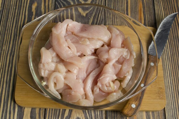 Searing chicken strips in a hot pan until golden brown for the Stroganoff base. Strips of chicken fillet being sautéed until golden in a black frying pan.