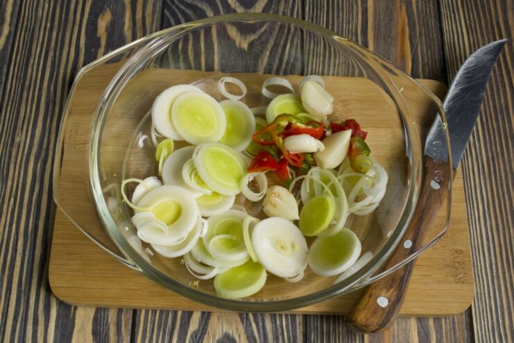Adding aromatics: leek, chili, and garlic cooking with chicken to build flavor. Chicken strips sautéing in a pan with sliced leeks, chili, and garlic.