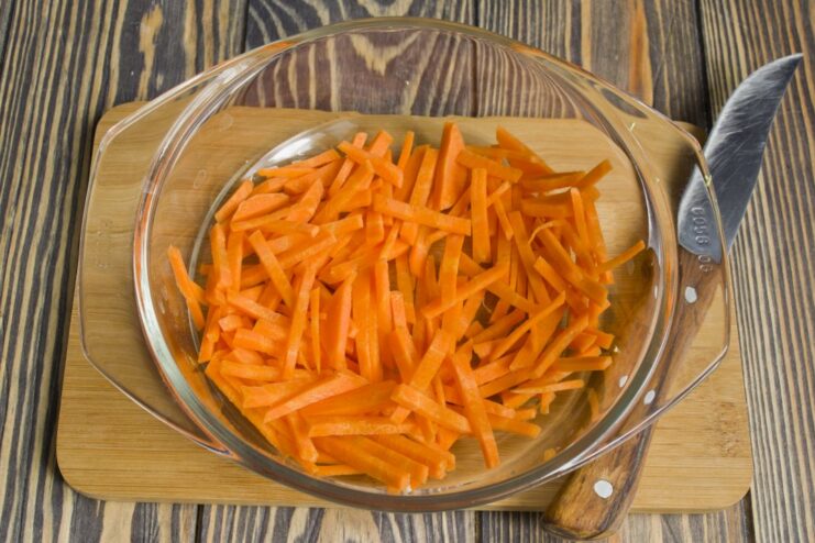 Incorporating grated carrots for sweetness and color into the chicken and leek mixture. Grated carrots being added to the pan with sautéing chicken and vegetables.