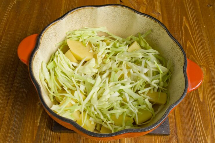 Building the Flavor: Adding Cabbage to the Stew Shredded white cabbage being added to the pan with potatoes.