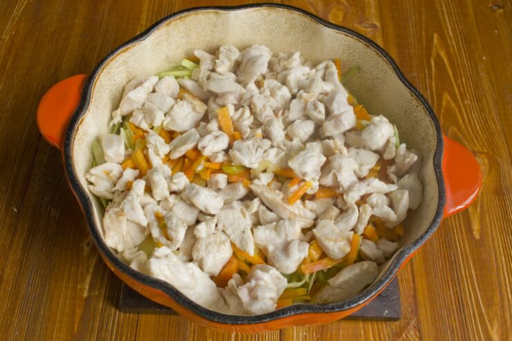 Layering the Chicken for a Tender Result Pieces of seared chicken fillet layered over the vegetables in the pan.