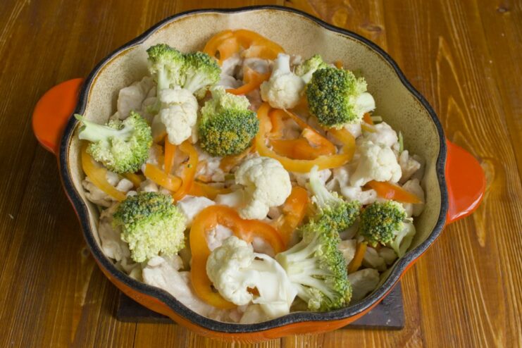 Adding the Final Vegetable Layer Before Simmering Bell pepper, broccoli, and cauliflower florets layered on top in the pan.