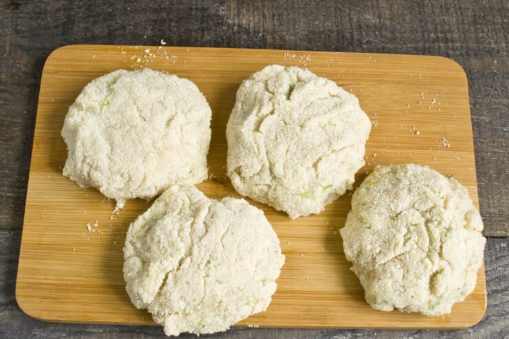 Coating the chicken patties in semolina for a crispy crust. Raw chicken patties being coated in a plate of semolina before frying.