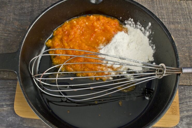 Creating the base for the sweet and sour sauce by cooking flour and tomato paste. Tomato paste and flour being cooked together in a pan to make a roux for the sauce.