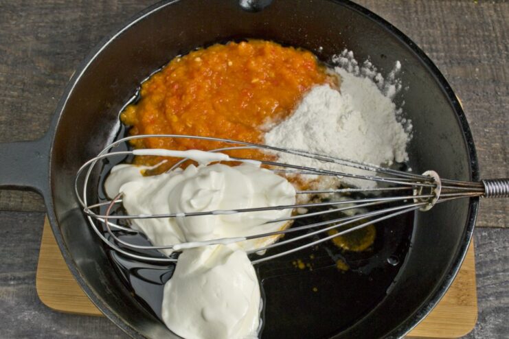 Whisking smetana into the sauce to make it creamy and rich. Smetana being whisked into the tomato base in a pan to create a creamy sauce.