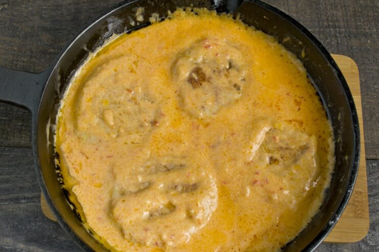 Simmering the fried chicken patties in the sweet and sour sauce to finish cooking. Fried chicken patties being placed into the creamy sweet and sour sauce in a pan.