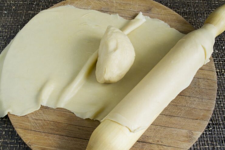 How to Roll Fresh Pasta Sheets for Lasagna A rolling pin rolling out a large, thin sheet of fresh pasta dough on a wooden surface.