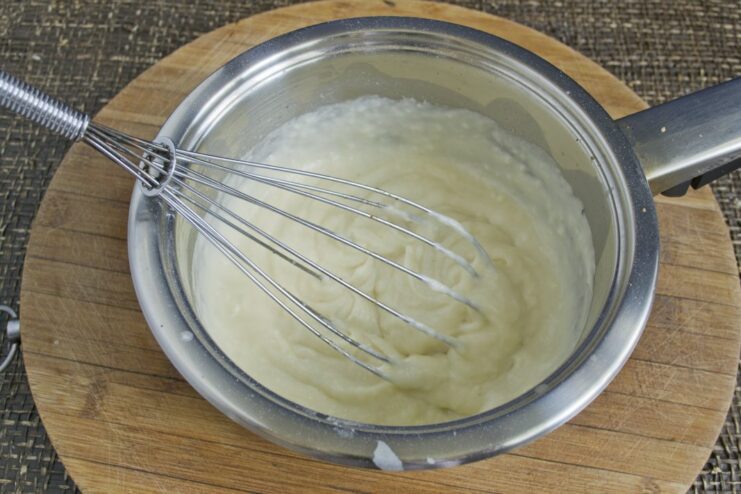 Making a Creamy Béchamel Sauce for Lasagna Whisking a creamy white béchamel sauce in a saucepan on the stove.