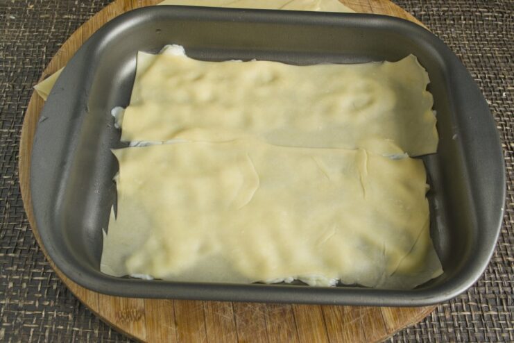 Starting the First Layer of Your Homemade Lasagna The first layer of lasagna being assembled in a baking dish with sauce and a pasta sheet.