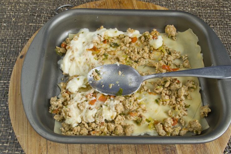 How to Layer Lasagna for Perfect Results Layering lasagna in a baking dish with meat filling, white sauce, and grated cheese.