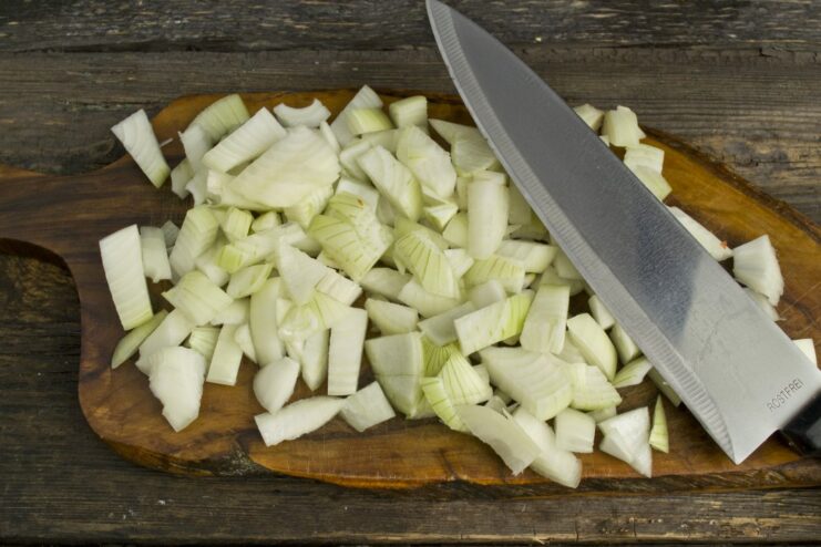 Close-up of hands dicing yellow onions on a cutting board.
