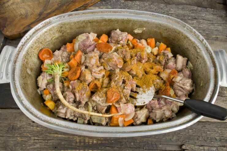 Spices being added to the sizzling meat and vegetables in the pot.