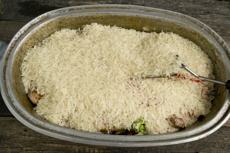 Soaked long-grain rice being spread evenly over meat and vegetables in a kazan.