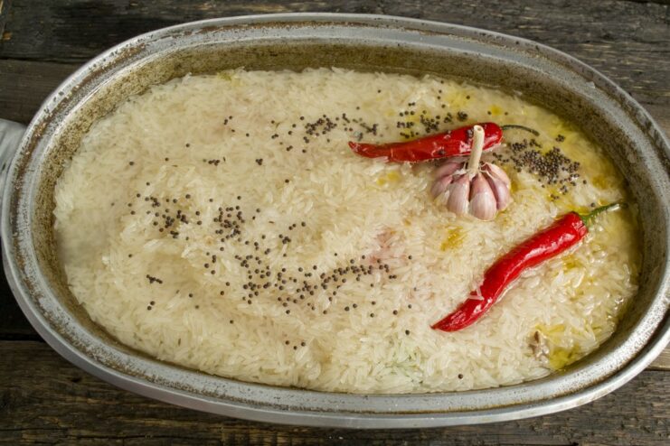 A whole head of garlic and chili peppers placed on top of the rice before adding water.