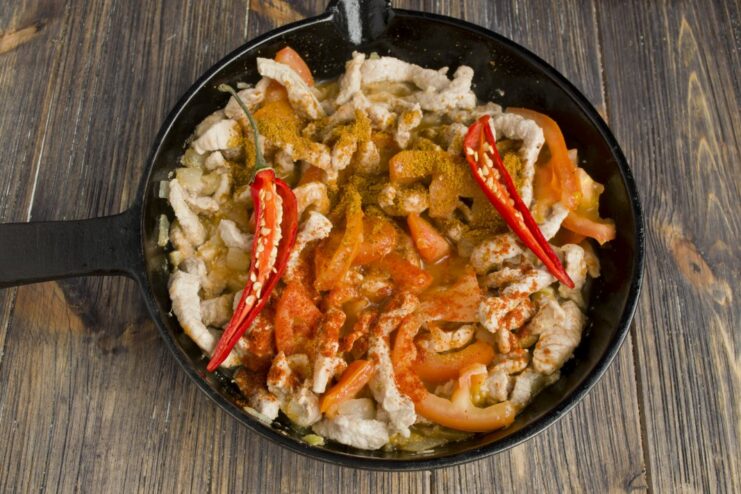 Seasoning the pork fajita filling with tomato puree, paprika, and chili Tomato puree, spices, and a whole chili pepper added to the pork filling in the pan.