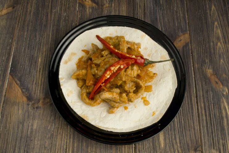Assembling the pork fajita: adding the filling to a warm tortilla Spoonful of pork and vegetable filling being placed onto a warm tortilla.