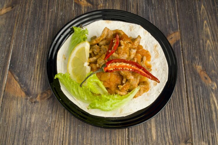 Delicious homemade Pork Fajitas served in a warm tortilla A plate of ready-to-eat pork fajitas wrapped in a tortilla with fresh greens.