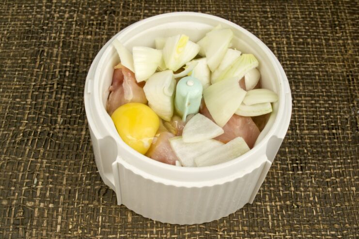 Blending chicken, egg, and onion for a smooth filling Chopped onion added to chicken and egg in a blender before mixing.