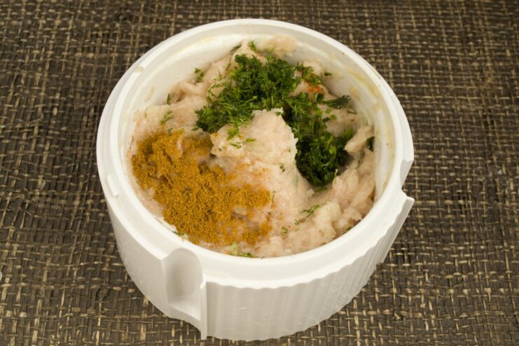 Seasoning the chicken filling with spices and fresh dill Ground chicken mixture in a blender bowl with spices and chopped dill on top.