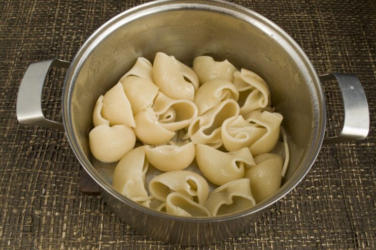 Parboiling large pasta shells before stuffing Large, gramophone-shaped pasta being boiled in a pot of water.