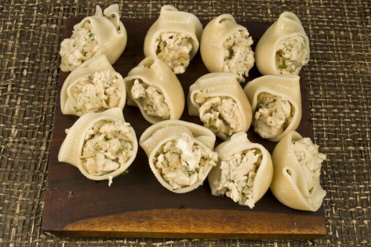 Filling the parboiled pasta shells with the chicken mixture A hand stuffing a large pasta shell with the cooked chicken filling.