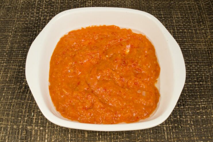 Creating a base of tomato sauce in the baking dish Pouring red tomato sauce into a white ceramic baking dish.