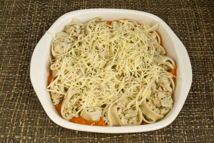 Topping the stuffed pasta with a generous layer of cheese Sprinkling grated hard cheese over the stuffed pasta in the baking dish.