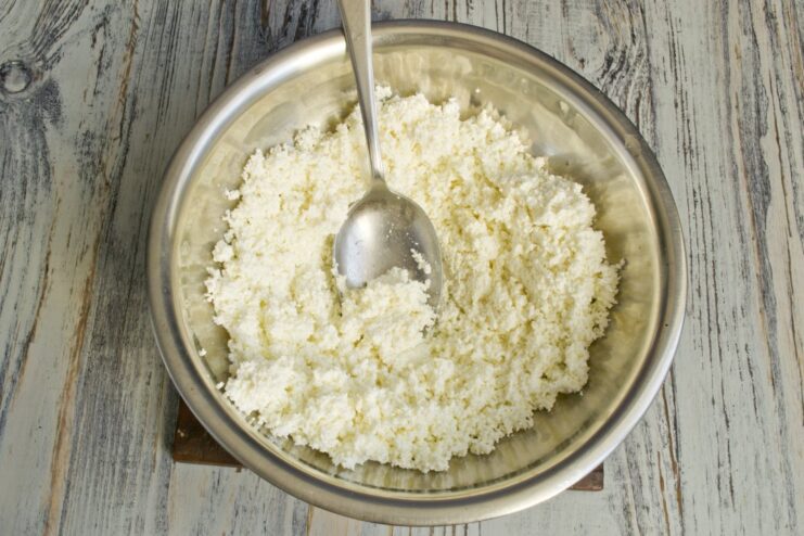 Tvorog (farmer's cheese) being pushed through a fine-mesh sieve into a bowl.
