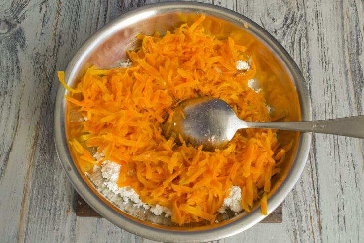 Sautéed grated carrots being added to the cheese and onion mixture.