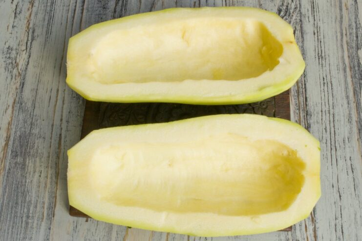 A zucchini cut in half, with seeds removed, being seasoned with salt.