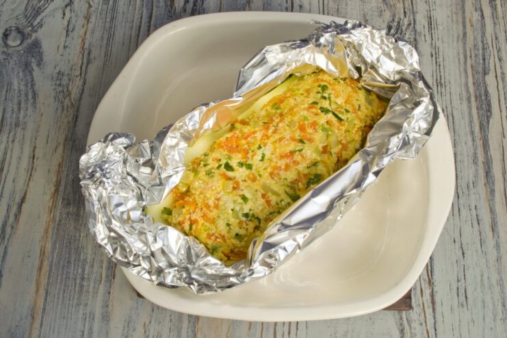 Stuffed zucchini halves being wrapped in aluminum foil before baking.