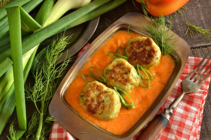 A white bowl filled with baked meatballs in a thick orange vegetable gravy, garnished with fresh herbs.