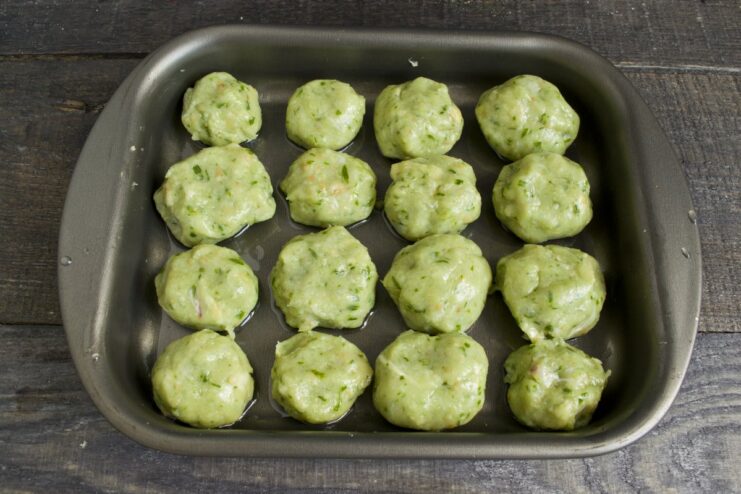 Raw chicken meatballs arranged on a greased baking sheet, ready for the oven.