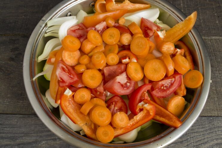 A sauté pan filled with chopped raw vegetables like zucchini, carrots, peppers, and tomatoes.