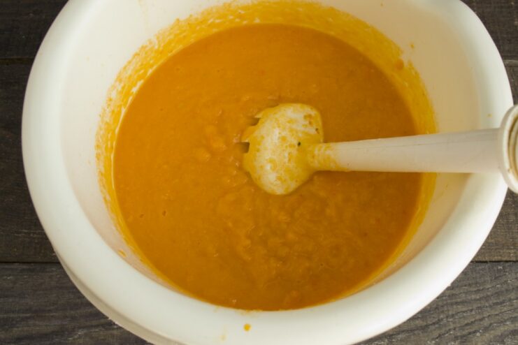 An immersion blender pureeing the cooked vegetables directly in the pan to create a smooth gravy.