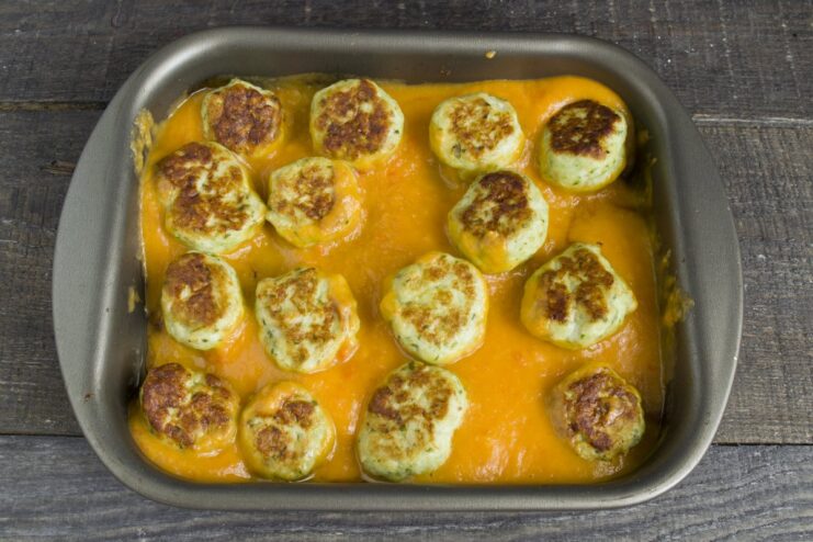 Smooth vegetable gravy being poured over baked meatballs on a baking sheet.