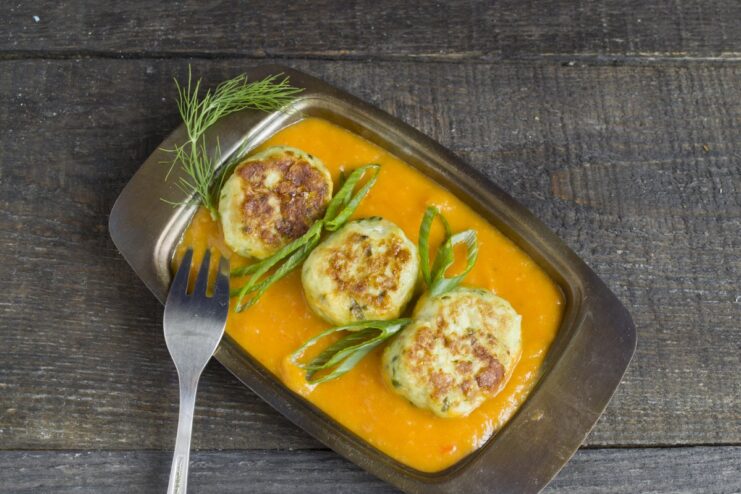 A close-up of the finished baked meatballs in vegetable gravy in a serving dish, garnished with parsley.
