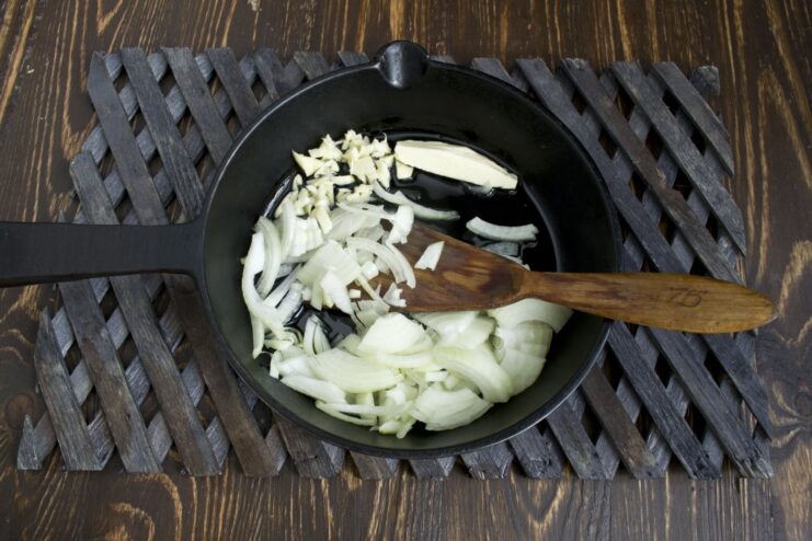 Sautéing finely chopped onions and garlic in a skillet until translucent Chopped onion and garlic being sautéed in a hot skillet with oil.