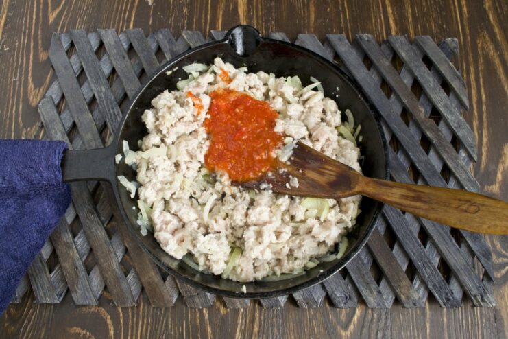 Stirring tomato purée into the browned meat and onion mixture Tomato purée being added to the ground meat and vegetables in the skillet.