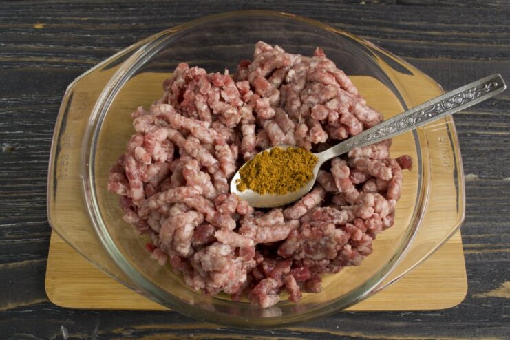 Searing the minced meat in a hot skillet with aromatic spices to build the first layer of flavor. Minced meat being fried with spices in a black skillet.