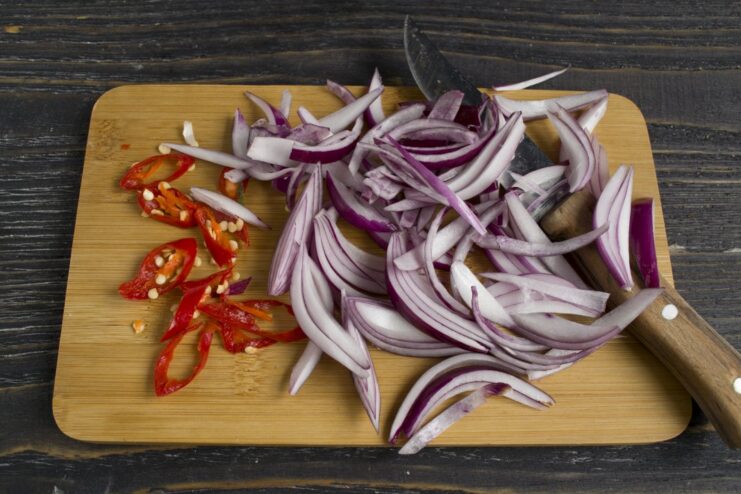 Adding freshly sliced chili and red onion to the minced meat for a kick of heat and sweetness. Sliced red onion and chili pepper being added to the frying minced meat in a skillet.