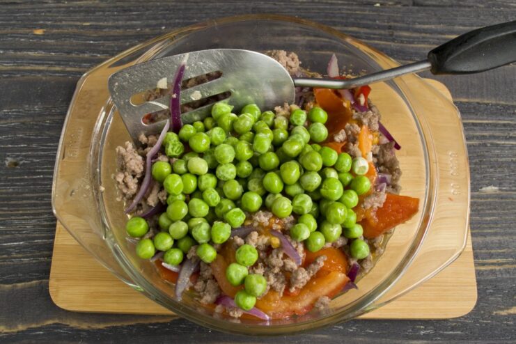 Finishing the filling by adding green peas and a flour slurry to thicken the sauce. Green peas and a flour mixture being added to the simmering minced meat filling in a skillet.