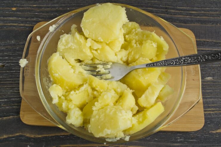 Mashing freshly boiled potatoes to create a smooth and fluffy base for the pie topping. Boiled potatoes being mashed with a potato masher in a bowl.