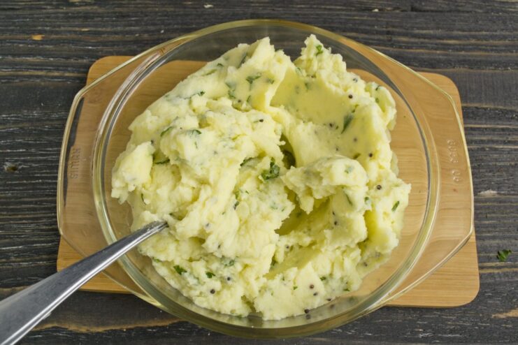 Enriching the mashed potatoes with butter, cream, and fresh herbs for a creamy and flavorful topping. Butter, cream, and chopped herbs being mixed into a bowl of mashed potatoes.