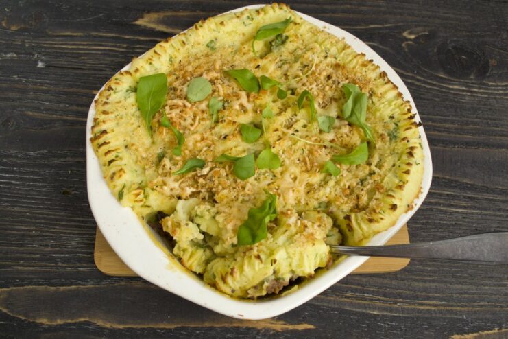 The potato pie baking in the oven until the top is golden brown and the filling is bubbly. The potato pie with minced meat and vegetables baking in the oven, with a golden-brown crust.