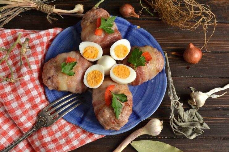 A plate of finished cheese-stuffed cutlets baked in bacon, garnished with herbs and quail eggs.